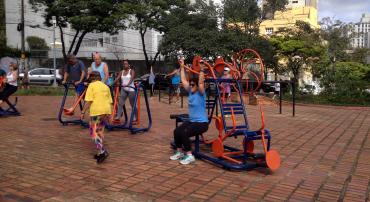 Grupo de adultos pratica atividades em aparelhos que compõe a Academia ao Ar Livre, projeto da Prefeitura de Belo Horizonte. Ao fundo, árvores e prédios.