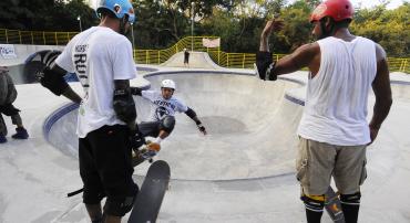 Dois skatistas estão mas margens e um realiza manobras no bowl da pista de skate do Parque Lagoa do Nado