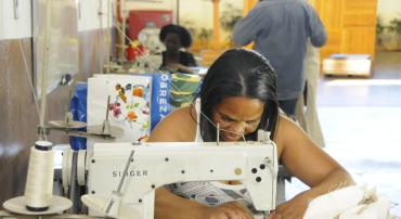 Mulher senta em mesa de costura.
