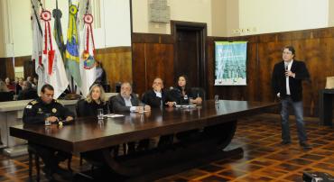 Secretário de Segurança, Cláudio Beato, de pé, com microfone. Na mesa, da esquerda para a direita, Rodrigo Prates, comandante da Guarda, Maria Caldas, secretária de Serviços Urbanos, Jackson Pinto, secretário de Saúde, o secretário Adjunto de Assistência Social e Maíra Colares, secretária de Políticas Sociais