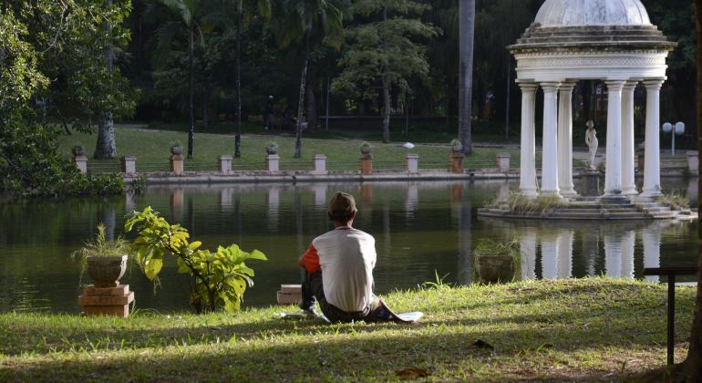 Cidadão sentado contempla lago no Parque Municipal Américo Renneé Giannetti.