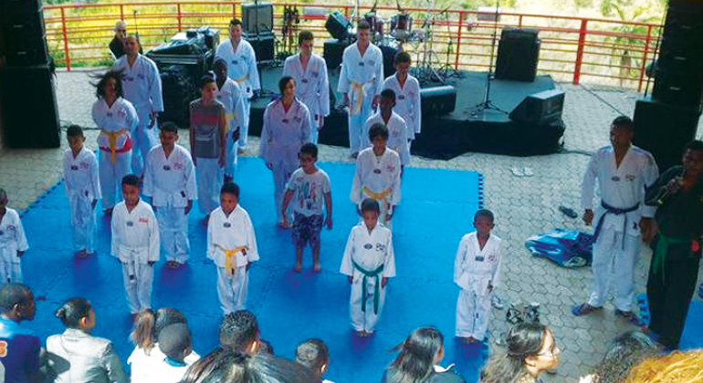 Cerca de quinze crianças praticam Tae-Kwon-Do em local coberto.