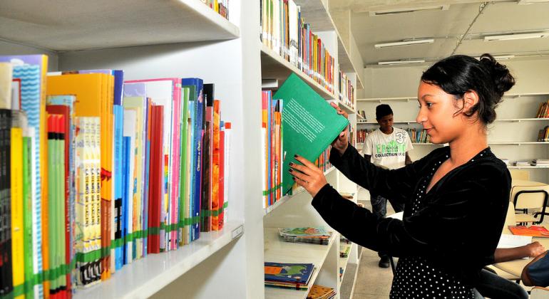 Menina mexe em livro em estante de biblioteca