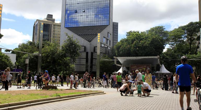 Mais de vinte pessoas interagem no cruzamento das avenidas Cristóvão Colombo e Getúlio Vargas; ao fundo, palco para apresentações e arranha-céu conhecido da Savassi e . 