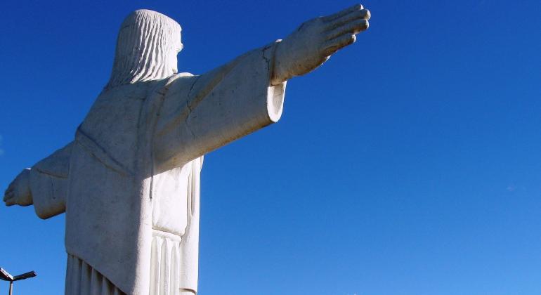 Imagem do Cristo do Barreiro de costas. Ao fundo, céu azul em dia claro.