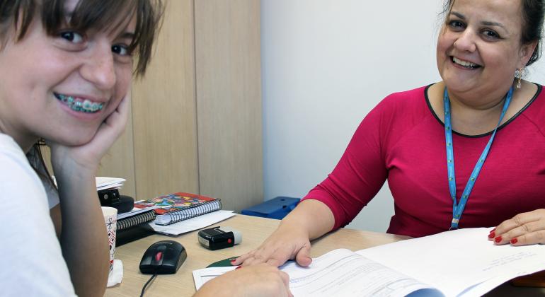 Estagiária sentada em frente a mesa de escritório; à frente, servidora da Prefeitura.