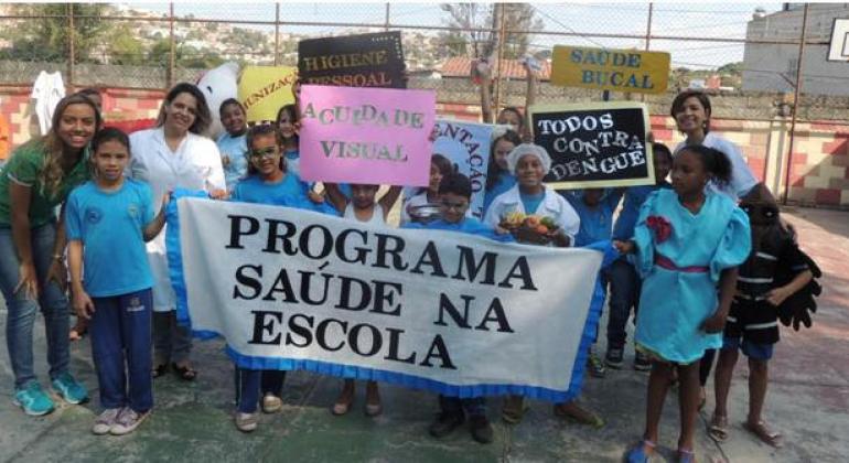 Um grupo de alunos e professores com cerca de dez pessoas empunham cartazes do Programa Saúde na Escola. Foto ilustrativa