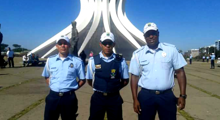 Três membros da Guarada Municipal à frente de igreja em Brasília. 