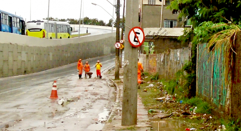 Cinco garis da SLU realizam limpeza calçada de avenida. 