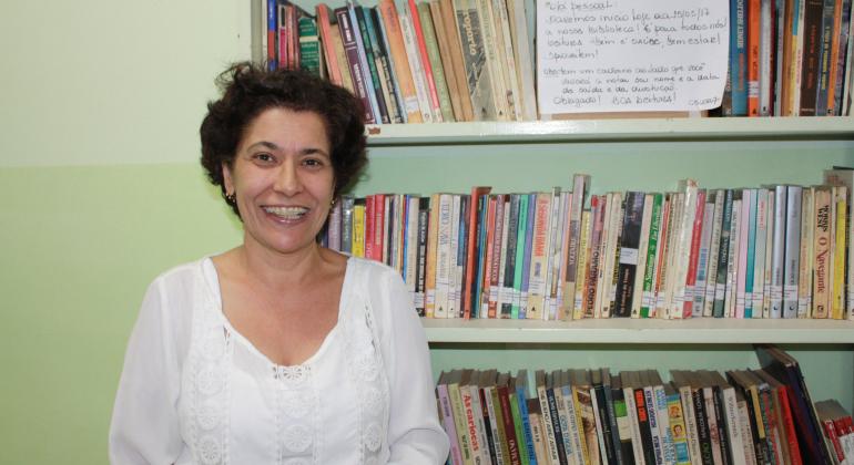 MUlher sorri à frente de estante com livros.