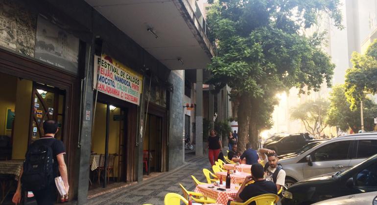 Mesas e cadeiras de bar em distância regulamentar de bares, deixando espaço na calçada para o trânsito de pessoas. 