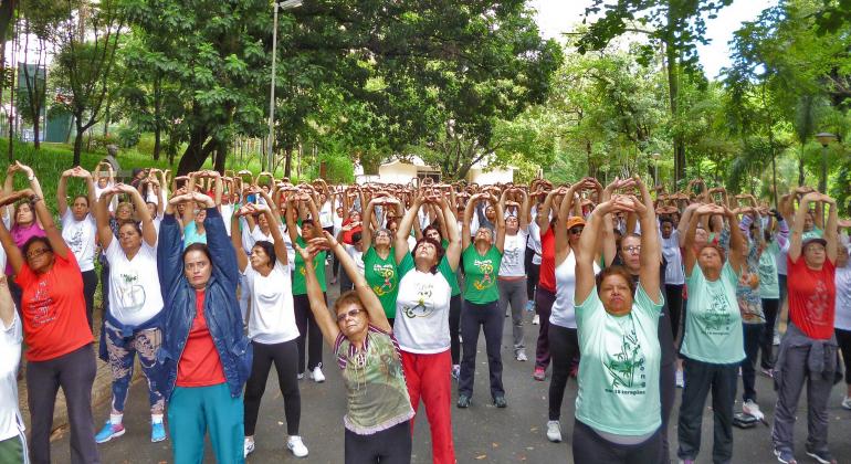 Mais de trinta pessoas em parque com as mãos levantadas fazendo movimentos de Liang Gong