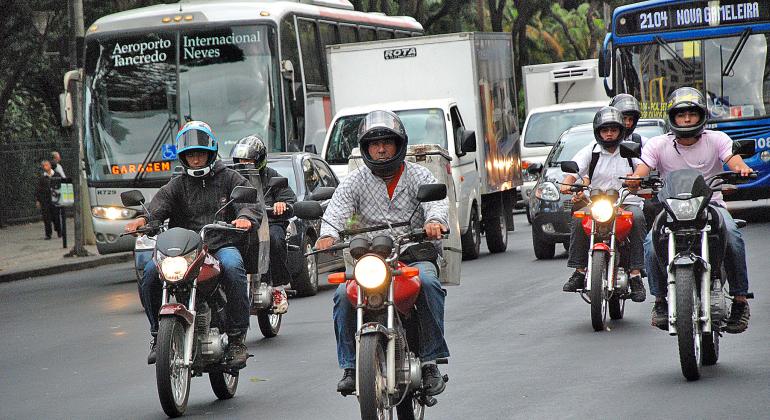 Cinco motocicletas andando em rua em dia de trânsito intenso. 