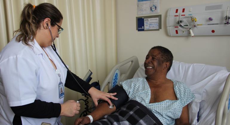 Médica mede a pressão de um paciente deitado.