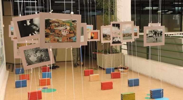 Mais de oito fotos do bairro Confisco, coladas em papelão pendurados no teto e fixados no chão com tijolos coloridos. 