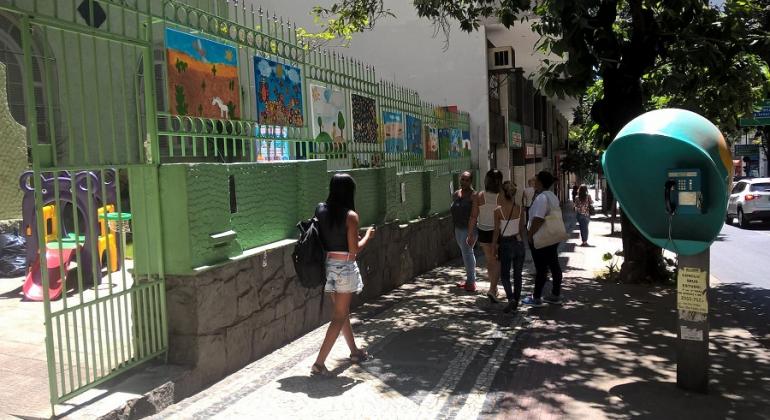 Dez telas pintadas por alunos em frente a E. M. Delfim Moreira; cerca de cinco passantes caminham pela calçada.