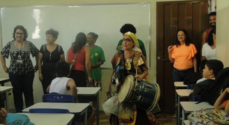 Mulher instrui alunos sobre coleta seletiva em escola municipal.