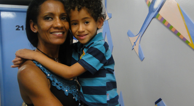 Mãe com filho no colo em Unidade de Saúde, ambos sorridentes.