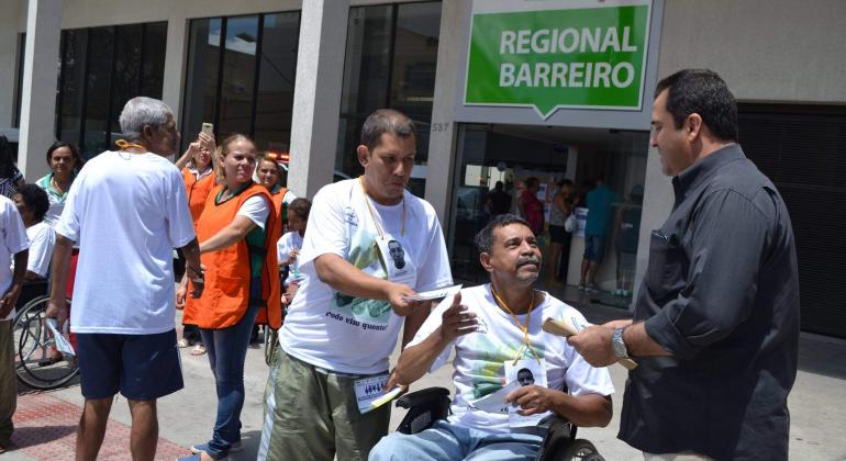 Cadeirante interage com dois homem na frente do Centro Dia Barreiro. 