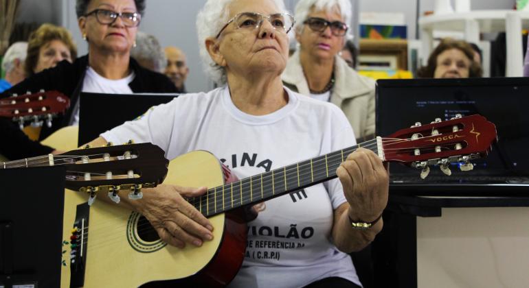 Idosa está sentada tocando violão