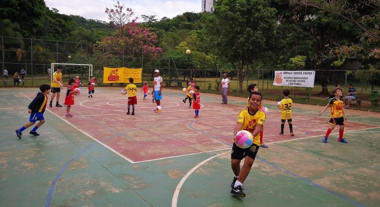 Crianças jogam futebol em quadra. 