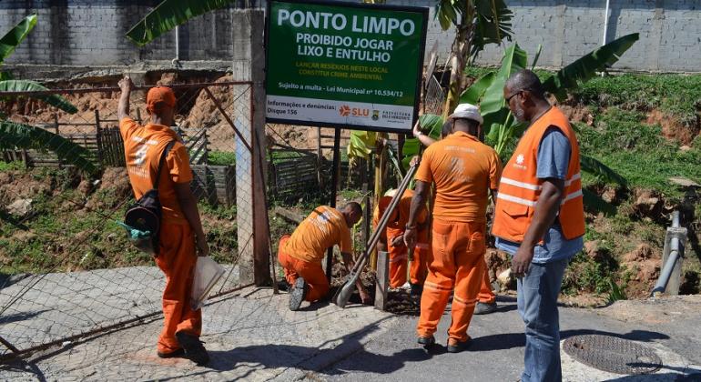 Cinco funcionários da SLU instalam placa de Ponto Limpo ao lado do córrego Aparecida