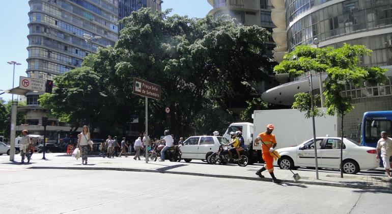 Gari limpa Praça Sete, ao fundo, carros e prédios. 