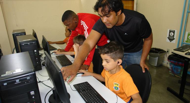 Dois técnicos da Prodabel ensinam duas crianças da Rede Municipal de Educação da PBH a acessar e utilizar computadores. 