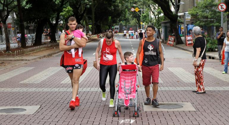 Dois homens, uma mulher e duas crianças caminham com um carrinho de bebê na Savassi. 