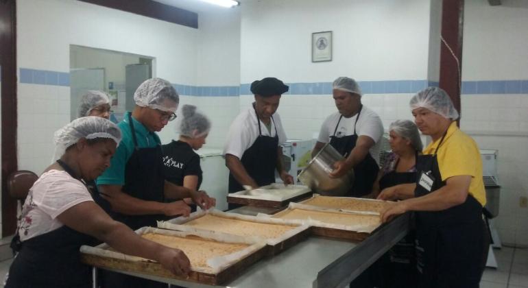 Sete pessoas arrumam quatro formas retangulares de bolo.