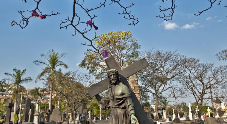 Túmulos e imagens do Cemitério do Bonfim. À frente, galhos de árvore e a imagem de Jesus Cristo carregando a cruz.