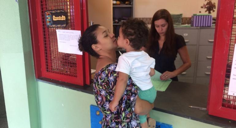 Mãe com filho no colo faz inscrição em escola infantil da Rede Municipal de Ensino. 