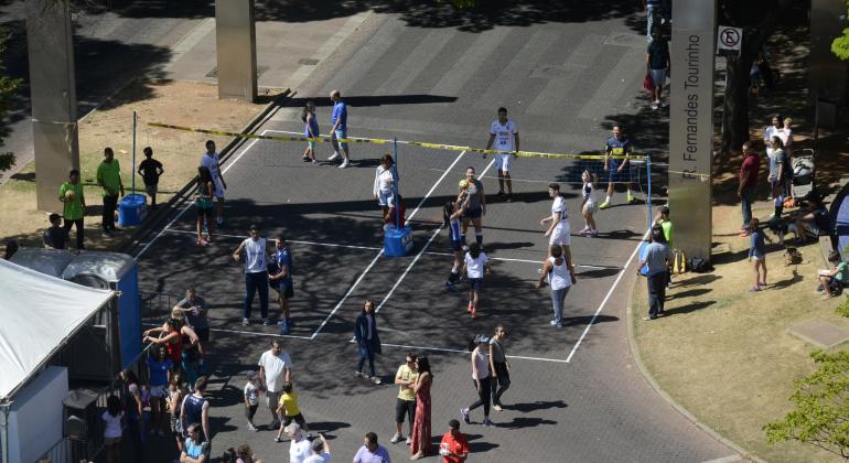 Quadra de volei montada com fitas no chão na Praça da Savassi. Dois times jogam na quadra.