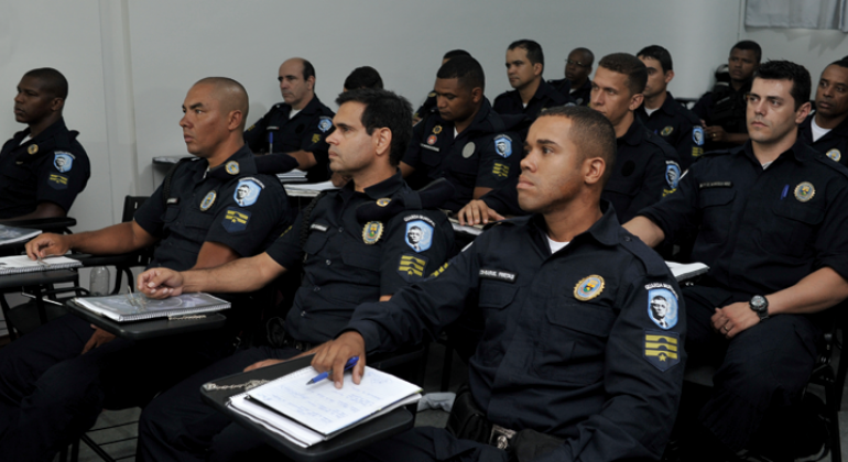 Mais de doze guardas municipais sentados em carteiras, fazendo curso de capacitação.