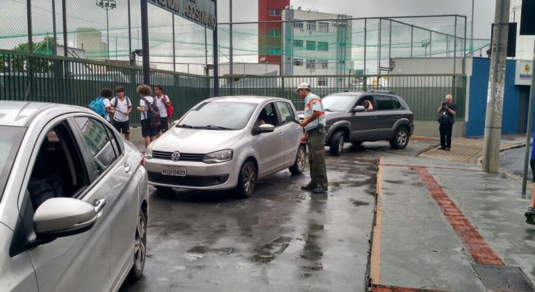 Operação volta às aulas. Três carros na imagem. Agente da BHTrans orienta um deles em frente a uma escola.