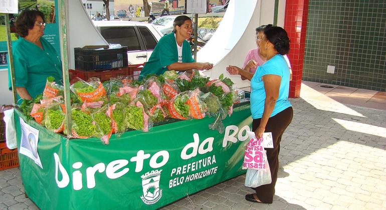 Duas mulheres compram alface hidropônica em barraquinha do Programa Direto da Roça.