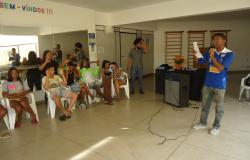 Jovem recita poesia. à direita, várias pessoas asssitem.