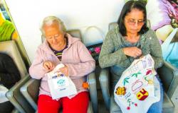 Uma senhora e uma mulher fazem bordados coloridos sentadas em poltronas.