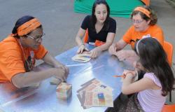 Quatro mulheres de diferentes idades, sentadas em uma mesa, fazendo oficina de reaproveitamento de papel.