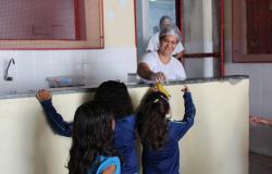 Três meninas na fila para a merenda enquanto uma funcionária entrega uma banana para uma delas