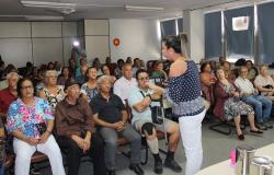 MUlher, de pé, palestra para cerca de trinta pessoas sentadas em sala. 