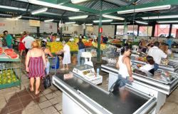 Sacolão ABC,l com muitas frutas e verduras e pessoas comprando. 