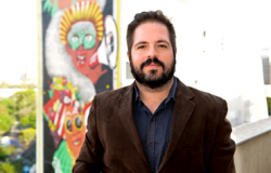 Gabriel Portela posa em frente a prédio com pitura artística. 